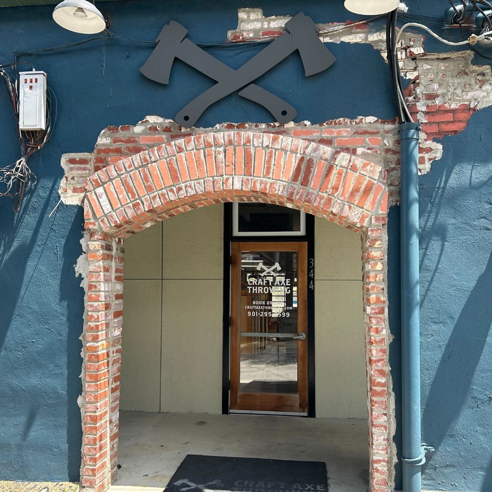 Brick-arched entrance to Craft Axe Throwing Memphis at 344 Floyd Alley, with a crossed-axes sign mounted on the blue wall above the door