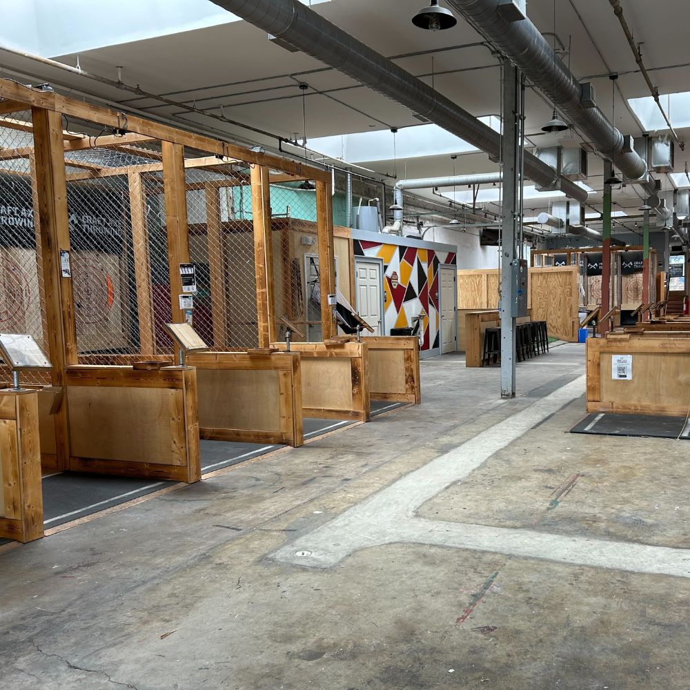Wood-framed axe throwing lanes with bullseye targets and lane-side counters inside Craft Axe Throwing Memphis, with a painted mural and bar stools at the far end
